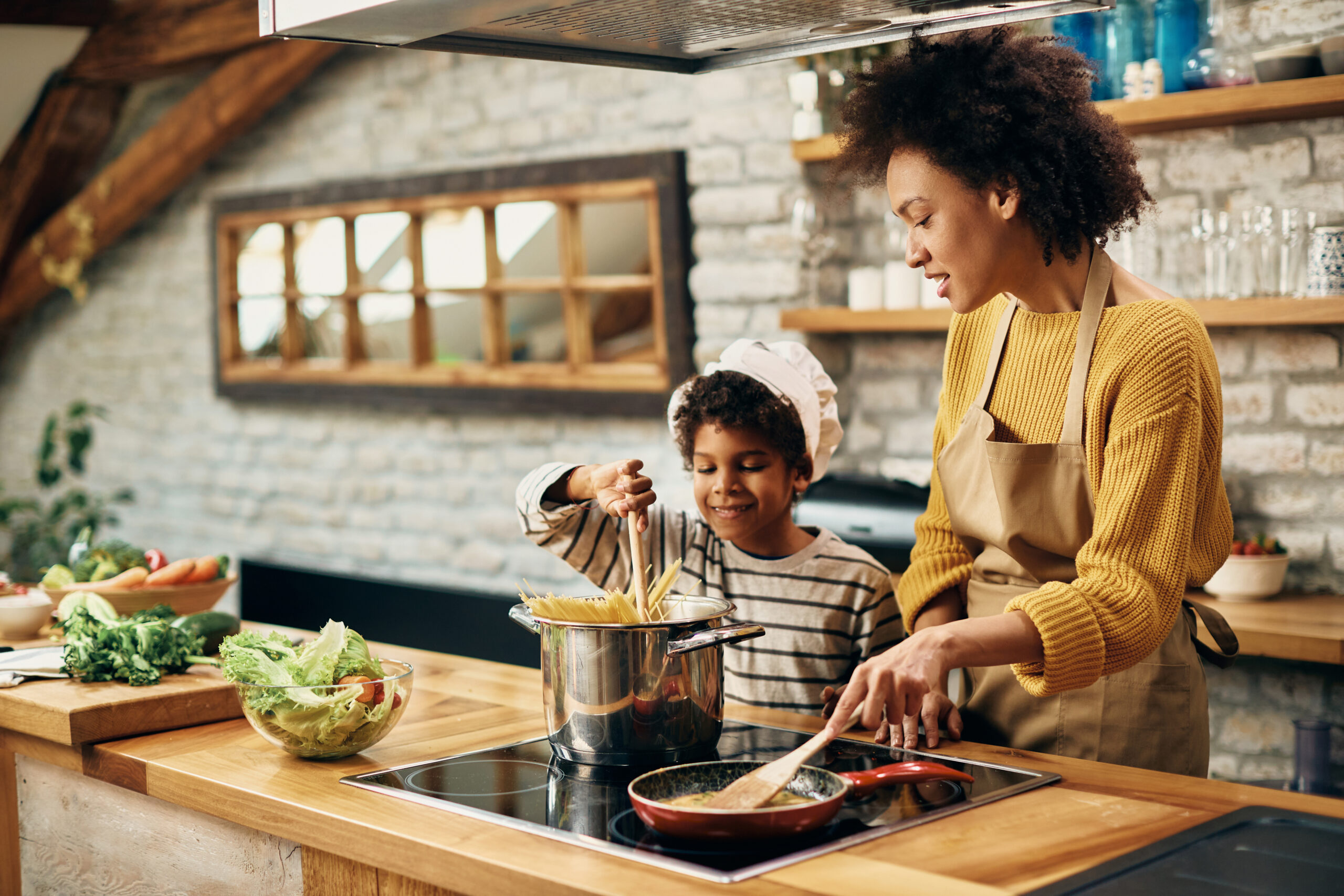 Small black boy preparing food with his mother in the kitchen.